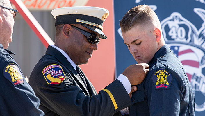 A fire academy cadet receives a pin from a CalFIRE captain at a graduation ceremony